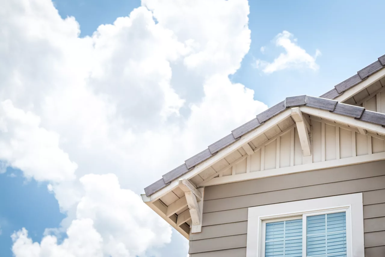 Angolo di casa con finestra e tetto con nuvole bianche e cielo blu sullo sfondo