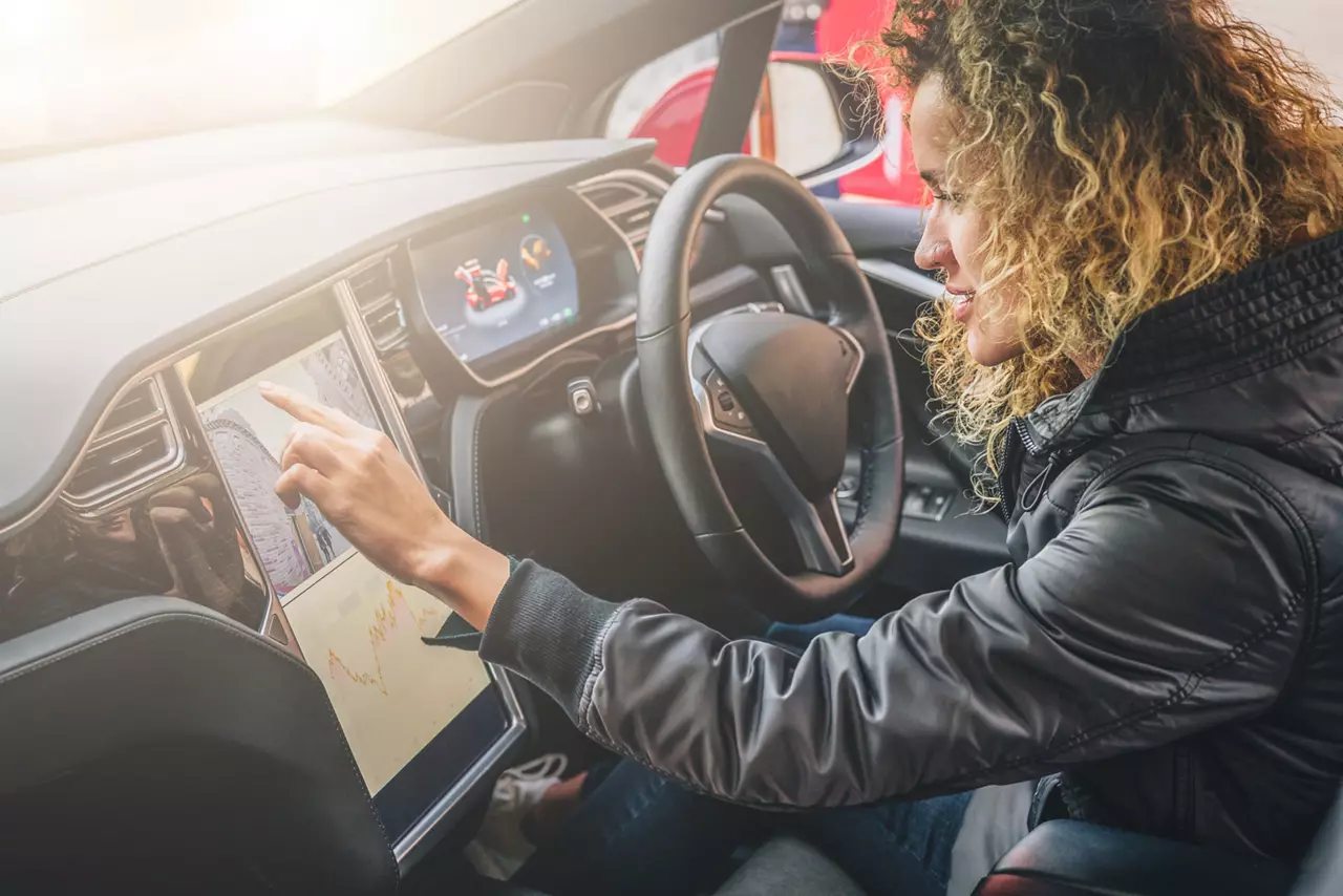 Woman sits behind wheel in car and uses electronic dashboard