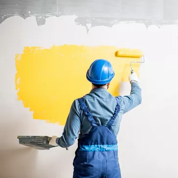 Arbeiter in Uniform beim Streichen der Wand mit gelber Farbe auf einer Baustelle in einem Gebäude