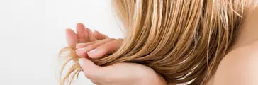 Young woman with hand touching her wet, blonde, perfect hair after shower on the white background. Care about beautiful, healthy and clean hair. Beauty salon concept. Side view.