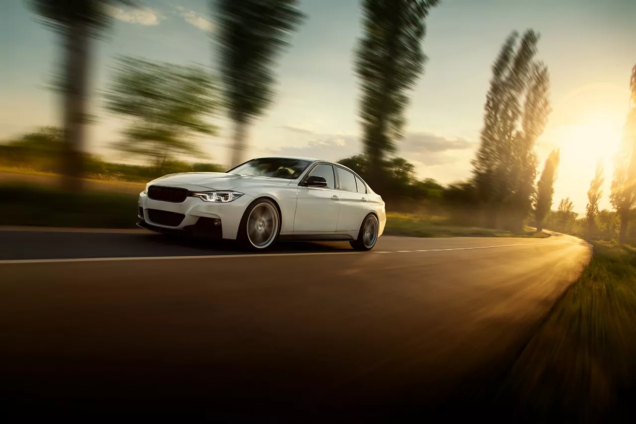 White car is driving on empty countryside asphalt road at sunset