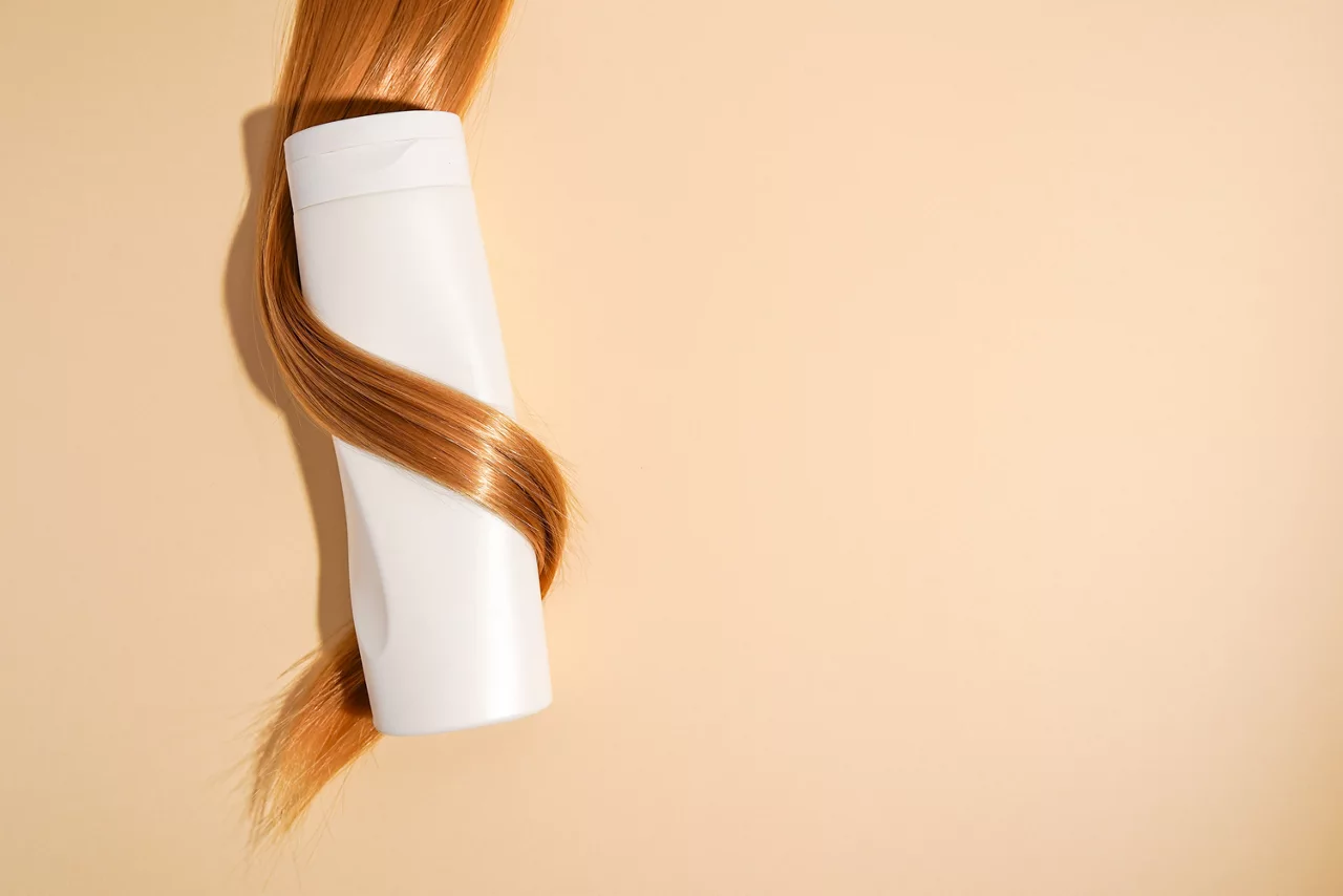 Capelli biondi arricciati intorno alla bottiglia di shampoo primo piano su sfondo chiaro, spazio copia