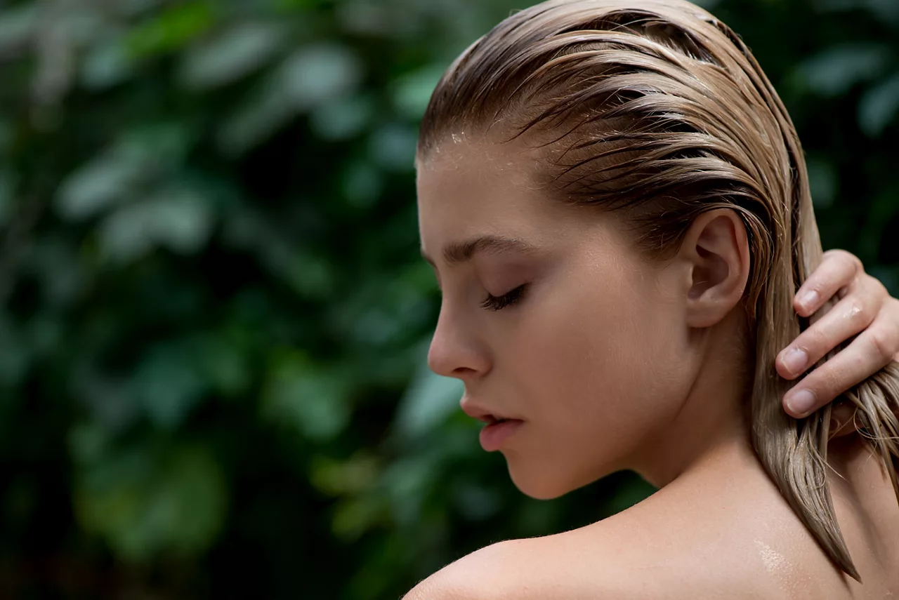 Una bella e giovane donna applica un balsamo, uno shampoo o un balsamo sui suoi capelli danneggiati