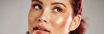 Woman, lips and lipstick application for beauty, cosmetics dermatology and skincare wellness in grey background. Female model, thinking face and lip gloss brush or makeup product for self care.